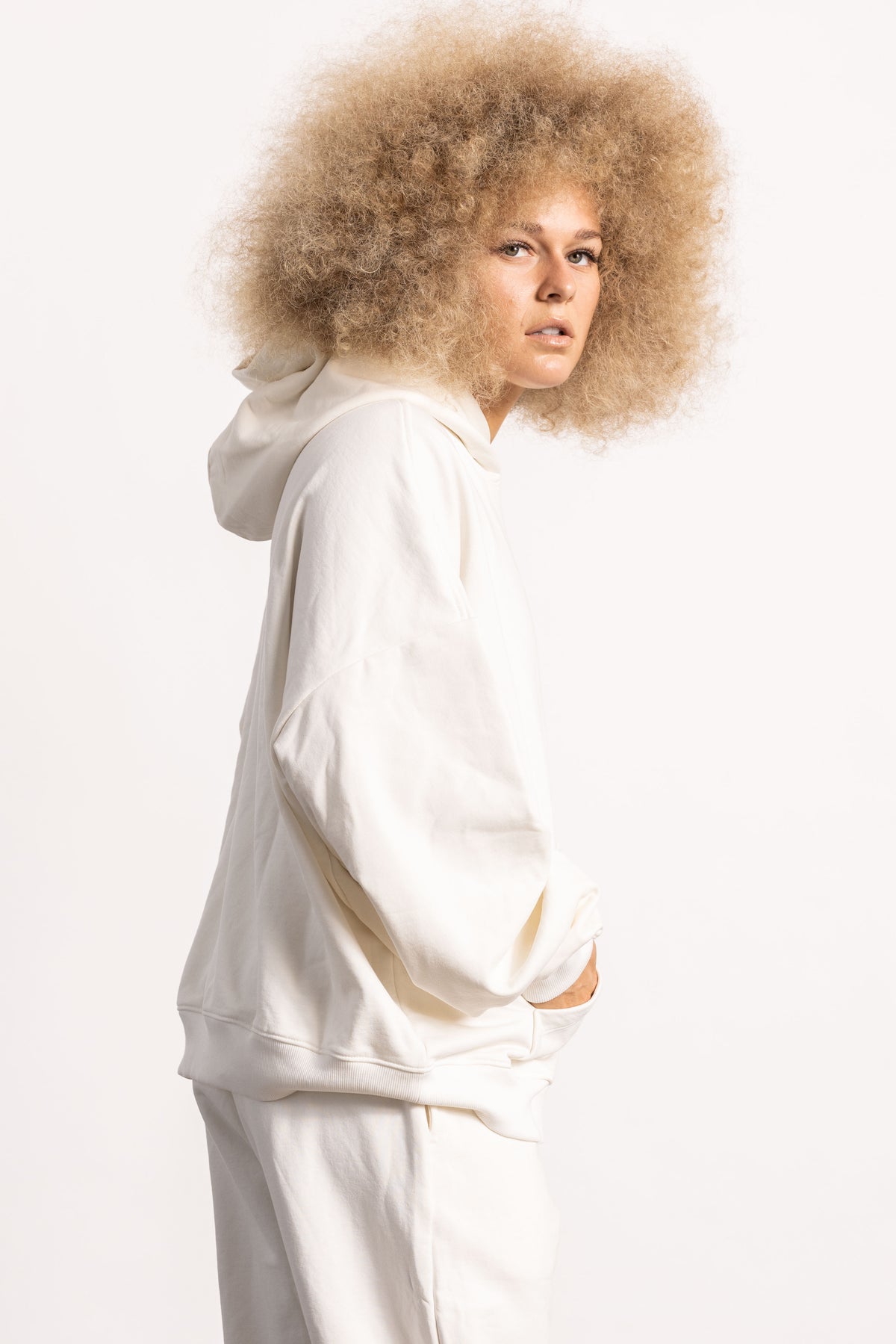 White blonde female model with edgy style wearing a off white drop shoulder pima cotton hoodie