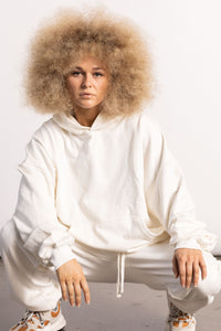 White blonde female model with edgy style wearing a off white drop shoulder pima cotton hoodie