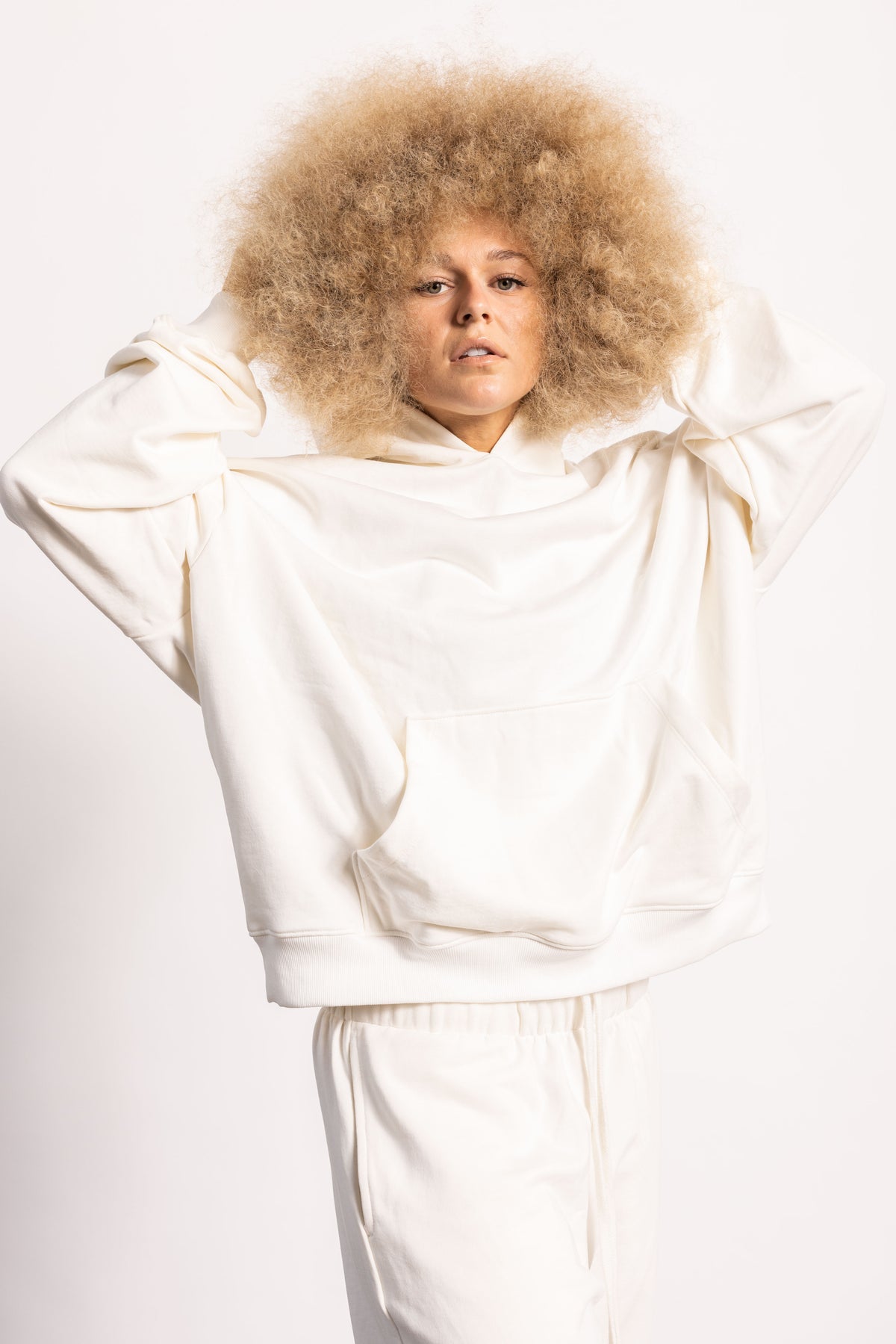 White blonde female model with edgy style wearing a off white drop shoulder pima cotton hoodie