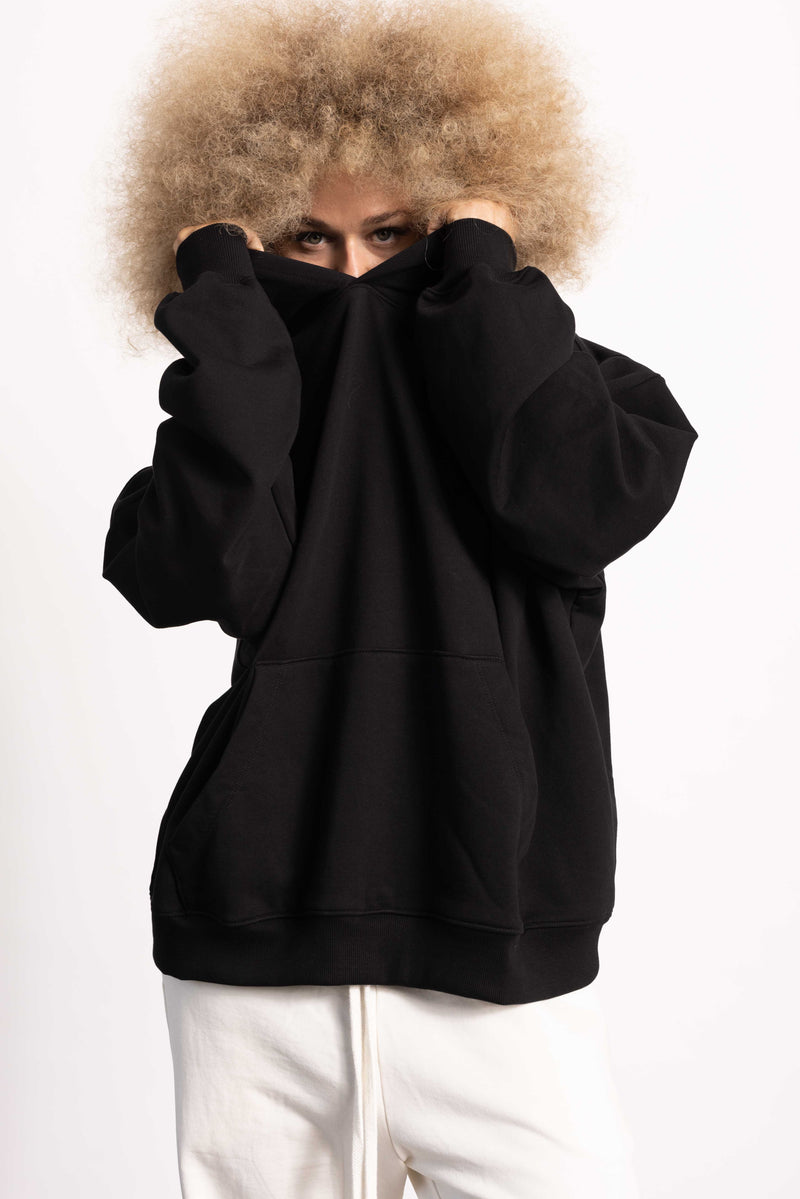 White female blonde model with edgy style wearing a black drop shoulder pima cotton hoodie